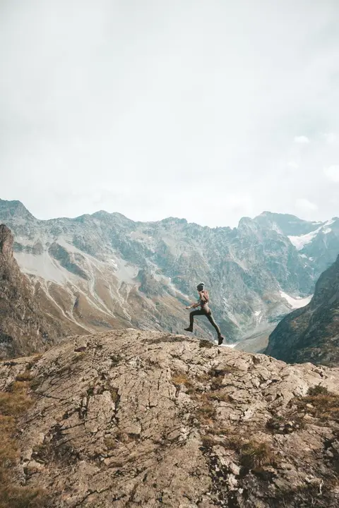 Mujer corriendo por la cima de una monta&ntilde;a con un valle de fondo